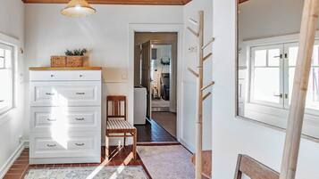 Een hal met een witte dressoir, een stoel, een houten ladder en een deur naar een andere kamer.
