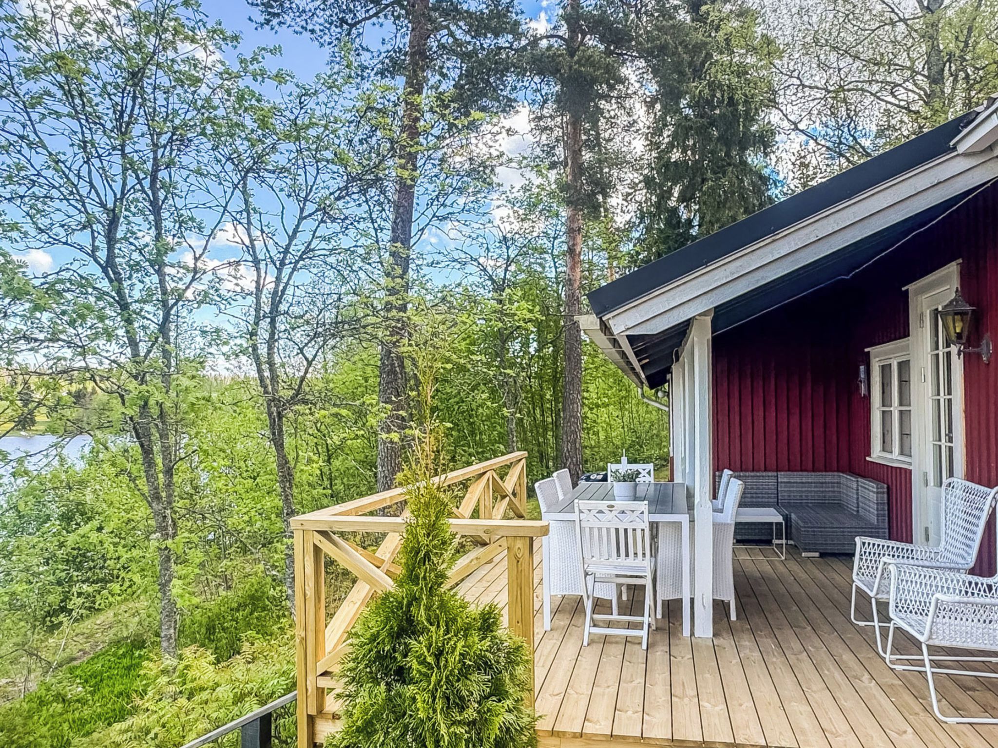 Une terrasse en bois avec des meubles d’extérieur, un bâtiment rouge et un paysage boisé en arrière-plan.