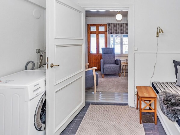 A laundry room with a white washing machine, a wooden chair, and a small table. - Punatulkku by Interhome (Somero)