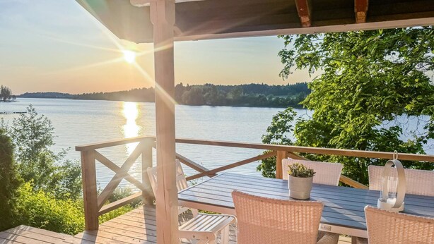 A wooden deck with wicker furniture overlooking a lake. - Punatulkku by Interhome (Somero)