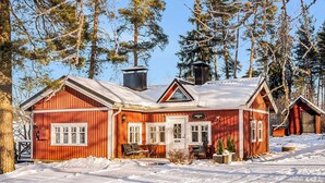 A red wooden cabin with a snow-covered roof, surrounded by trees. - Punatulkku by Interhome (Somero)