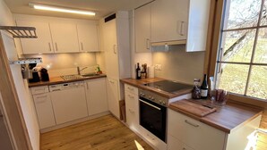 Una cocina moderna con armarios blancos, horno de acero inoxidable, lavavajillas integrado y un amplio ventanal que proporciona luz natural.