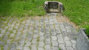 Un sendero pavimentado que conduce a una edificación de piedra rodeada de césped.