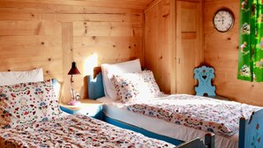 A wooden cabin room with two beds, a clock, and a green curtain. - Sonnenfreude, Chalet by Interhome (Schönried)