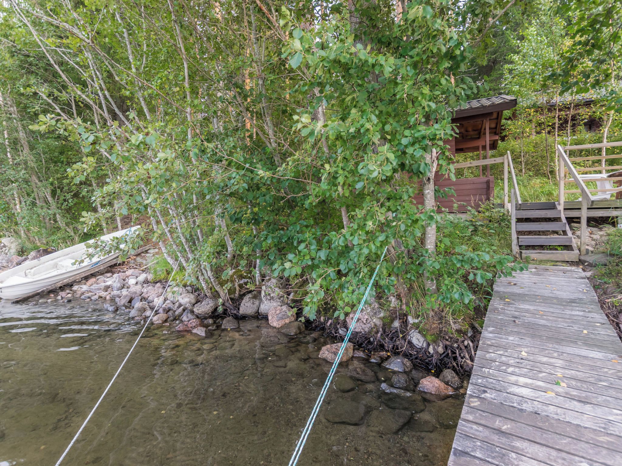 Une jetée en bois s’avance dans un ruisseau aux eaux claires, et une petite construction en bois se trouve sur la droite.