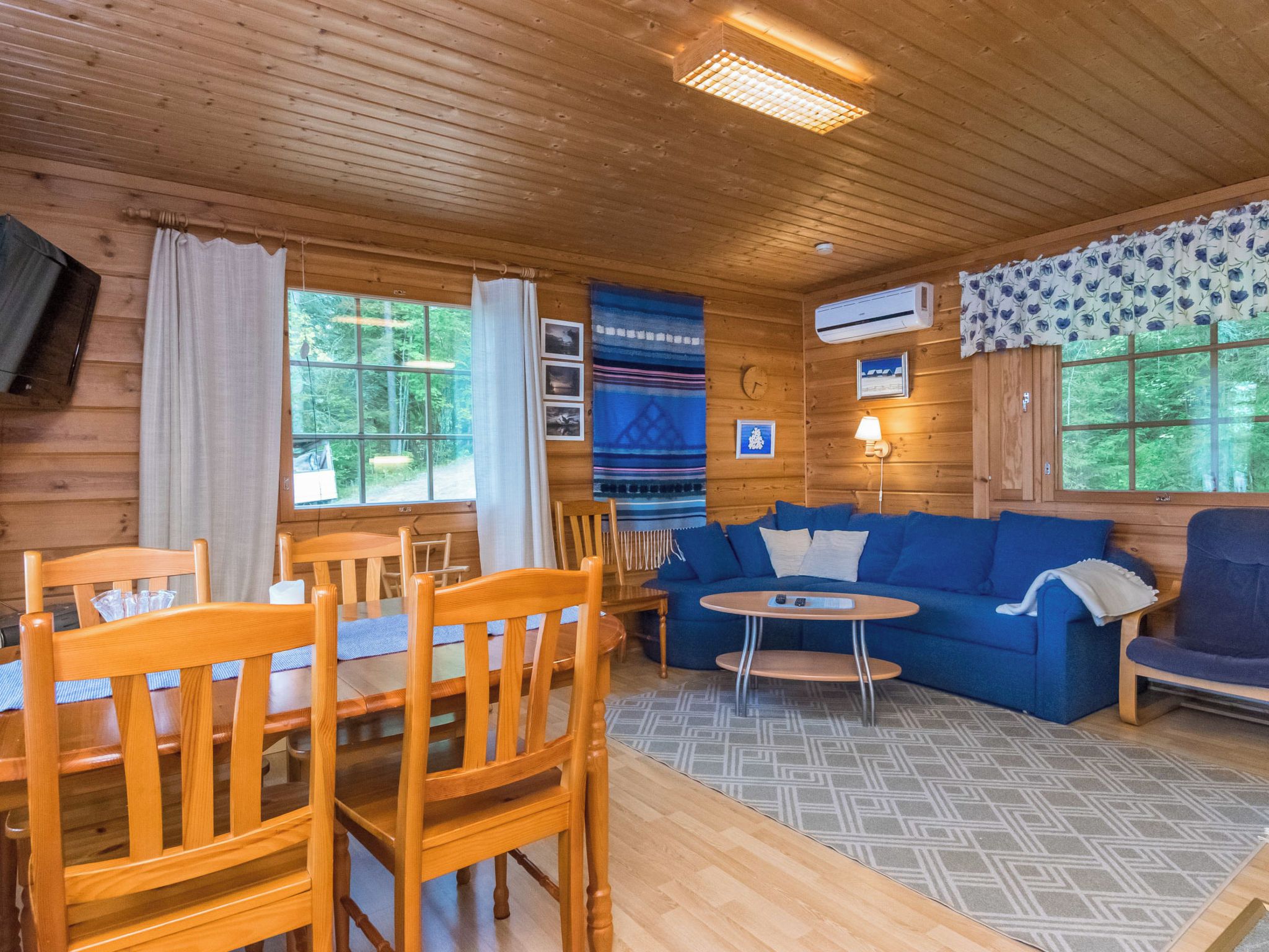 A wooden cabin interior with a dining table, chairs, a sofa, and a small round table.
