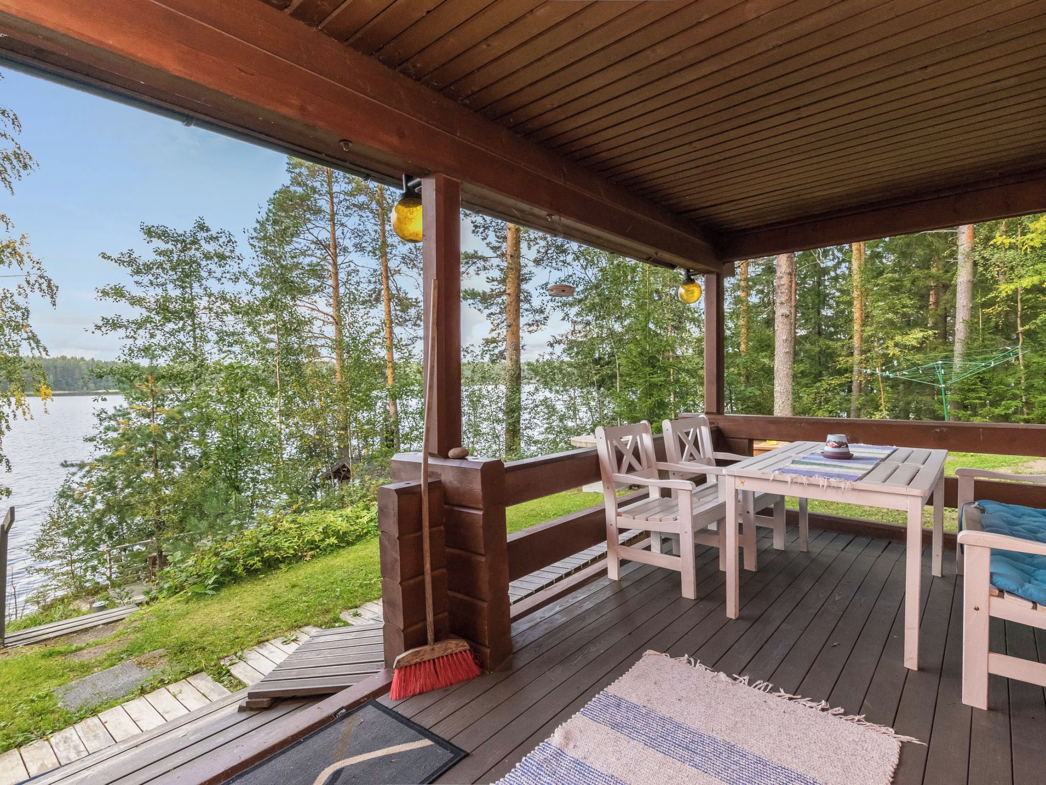 A covered outdoor deck with a table and chairs, overlooking a body of water and surrounded by trees.
