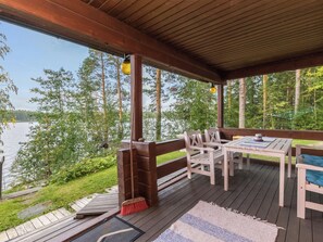 A covered outdoor deck with a table and chairs, overlooking a body of water and surrounded by trees. - Illanvirkku by Interhome (Punkaharju)