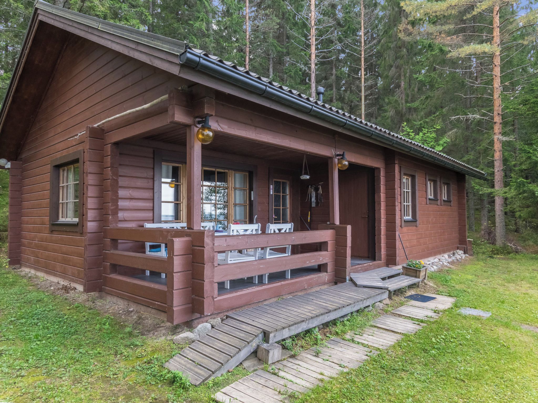 A wooden cabin with a porch, steps leading to the entrance, and a surrounding forest.