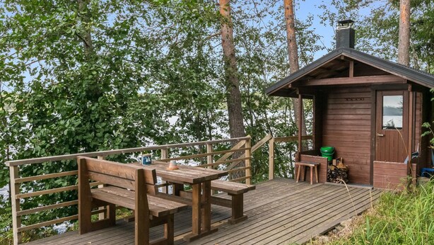 Een houten terras met banken en een klein huisje met schoorsteen.