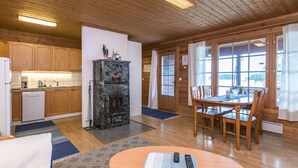 Een gezellig interieur van een chalet met houten vloeren, een eethoek met tafel en stoelen, een keuken met houten kastjes, en een open haard.
