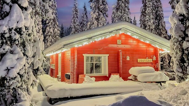 A snow-covered cabin with a red exterior and a sign reading "JOUTILAS".