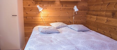 A wooden-paneled room with a bed, two bedside lamps, and a shelf with books.