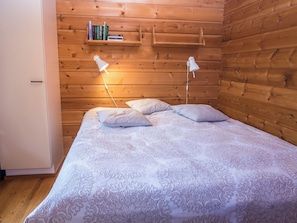 A wooden-paneled room with a bed, two bedside lamps, and a shelf with books. - Joutilas by Interhome (Kuusamo)