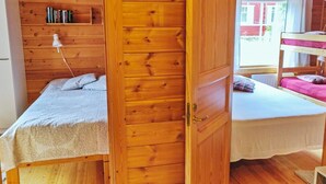A wooden cabin room with two beds, a bookshelf, and a window.