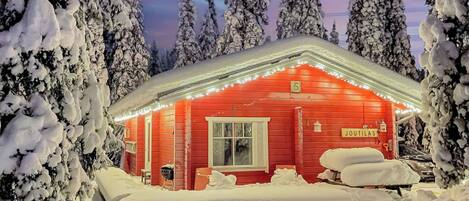 A snow-covered cabin with a red exterior, a window, and a door.