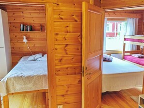 Una habitación de madera con dos camas, una estantería con libros y una ventana.