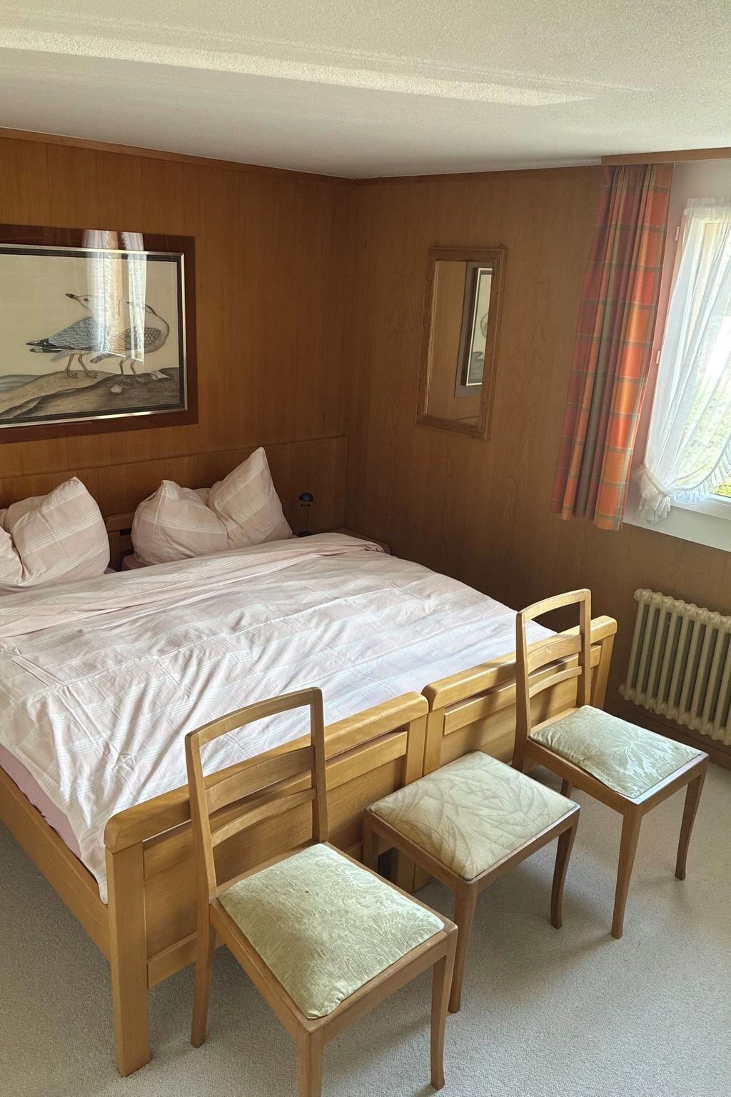 Un dormitorio con una cama grande, dos sillas de madera, un cuadro en la pared y una ventana con cortinas.