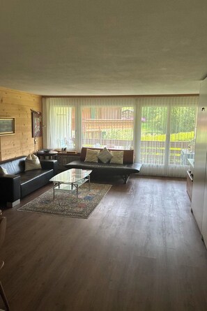Ein geräumiges Wohnzimmer mit großem Fenster, einer Sofagarnitur, einem Couchtisch und einem Teppich.