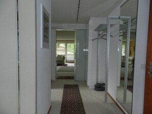 Un pasillo con alfombra, una puerta que da a una habitación con cama y una puerta de vidrio que refleja otra habitación.
