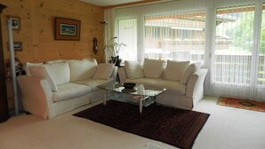 Una sala de estar con un sofá color beige, una mesa de centro de vidrio y un tapete oscuro.