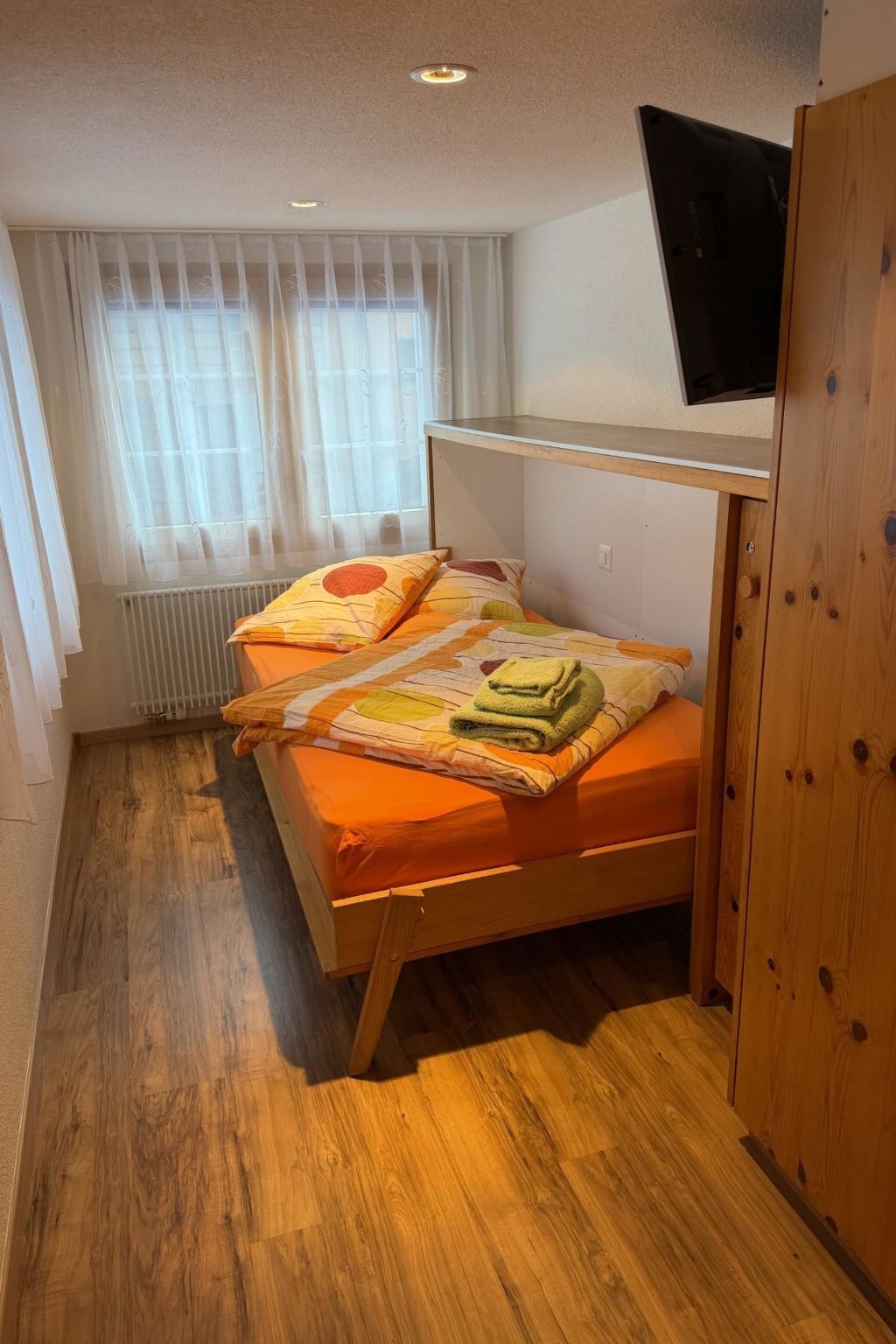 A small, cozy room with a bunk bed, a radiator, and a window with sheer curtains.