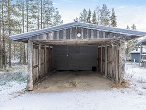 Un garage en bois avec un toit en métal, entouré d’un paysage enneigé et d’arbres.
