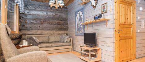 Ein Holzblockhaus-Innenraum mit einer Couch, einem Sessel, einem Fernseher und einem an der Wand befestigten Radio.