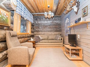 A log cabin interior with a sofa, armchair, television, and wooden shelves.