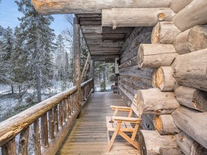 A wooden deck with a railing, leading to a log cabin with a view of snow-covered trees.