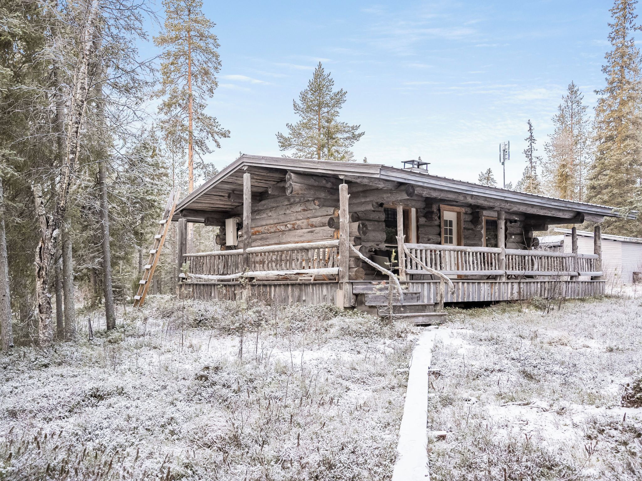 Une cabane rustique en rondins de bois, dotée d’un porche, entourée d’un paysage enneigé et d’arbres.