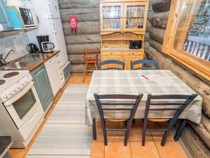 A cozy cabin-style kitchen with a dining area, wooden cabinets, and a view through a window. - Pajalan honka by Interhome (Kuusamo)