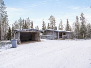 Une cabane dotée d’un garage fermé et d’un porche, entourée d’arbres couverts de neige.