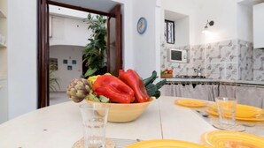Ein Essbereich mit einem Tisch für zwei Personen, mit gelben Tellern und klaren Gläsern. Auf dem Tisch steht eine Schüssel mit Gemüse, und an der Wand ist eine Uhr zu sehen.