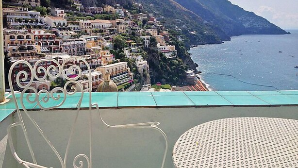 Eine Küstenstadt mit terrassenförmig angeordneten Gebäuden, einem Balkon mit Metallgeländer und Blick auf das Meer.