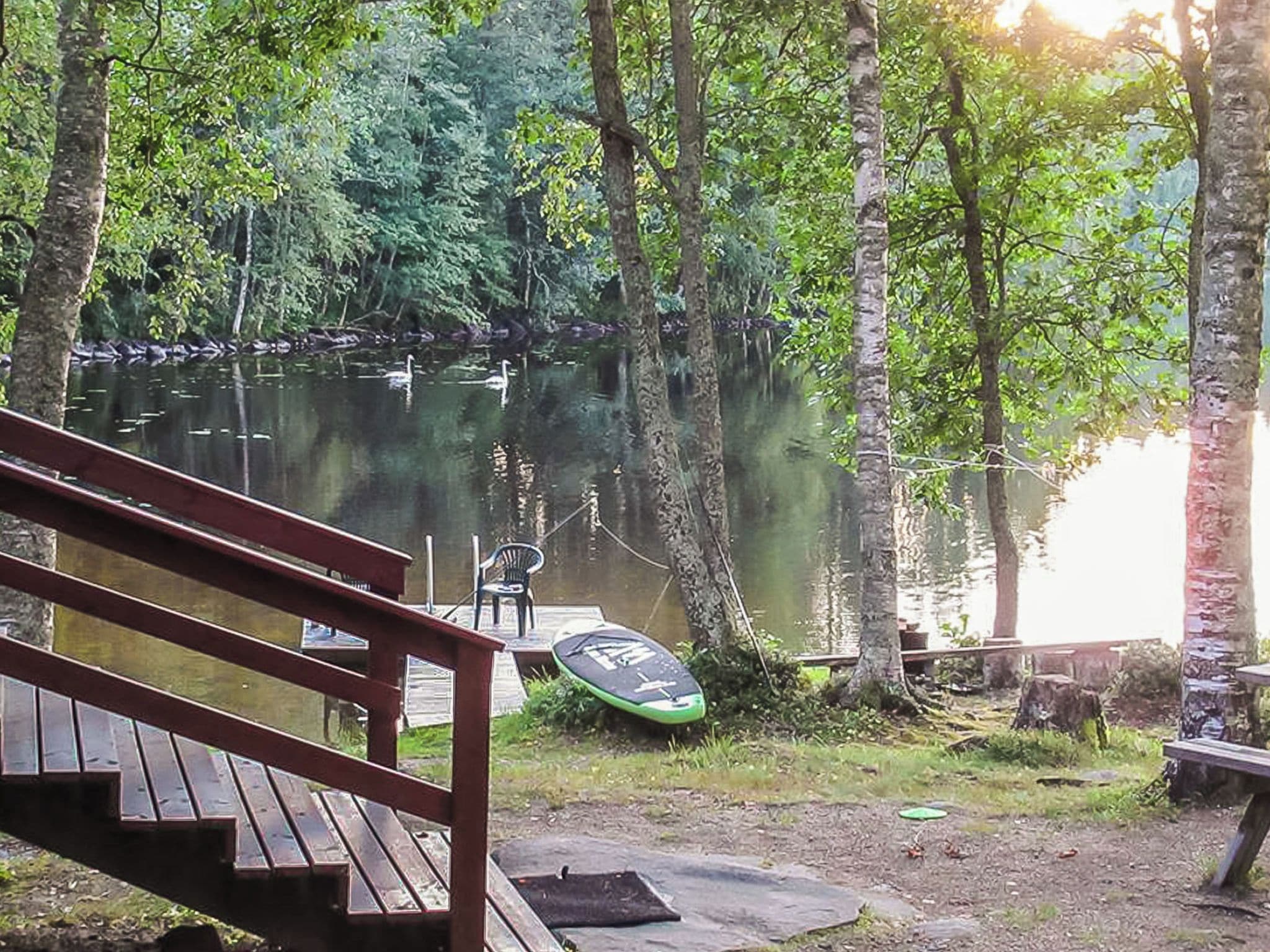 A wooden deck leading to a calm lake surrounded by trees.
