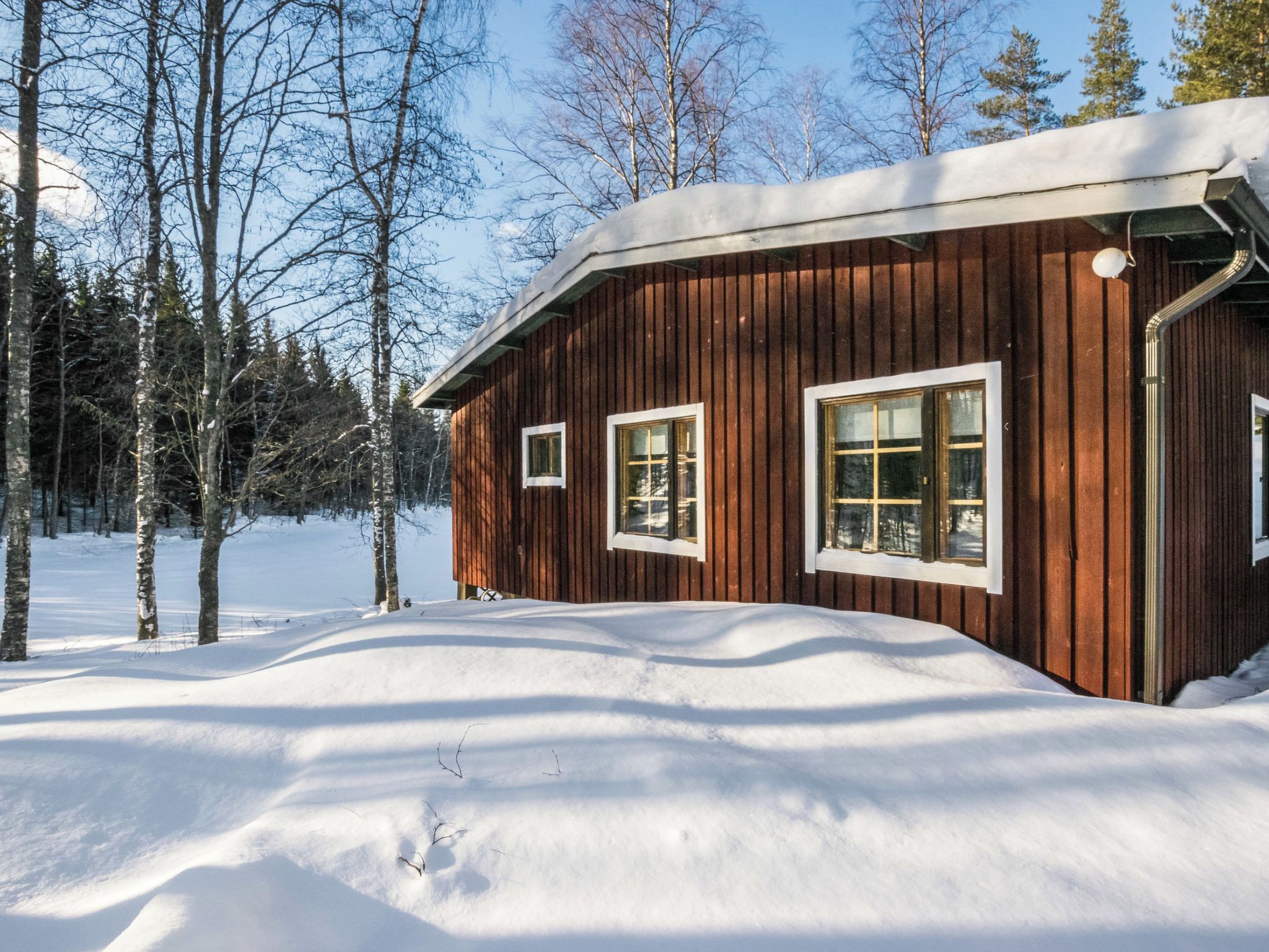 Una baita di legno con un tetto imbiancato dalla neve, circondata da alberi e da un paesaggio innevato.