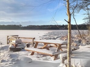 Un lac gelé, avec des tables de pique-nique en bois recouvertes de neige, entouré d’arbres et surplombé d’un ciel dégagé.