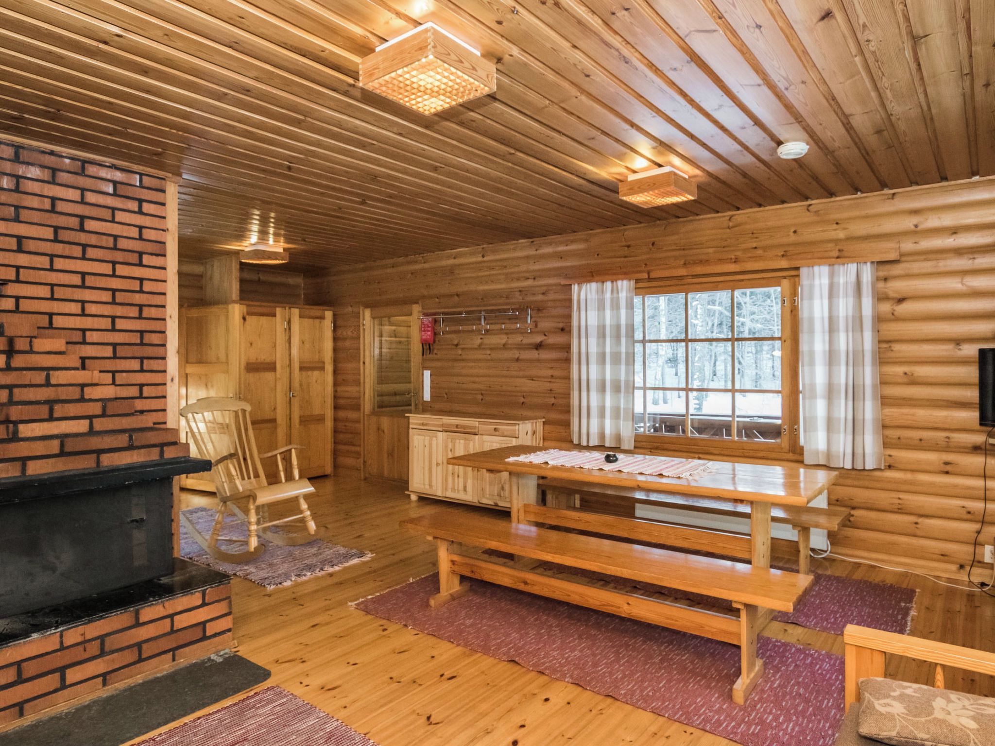 A cozy cabin interior with a fireplace, wooden walls, a dining table, and a rocking chair.