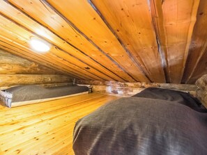 A small, wooden attic bedroom with a sloped ceiling, a single bed, and a small window.