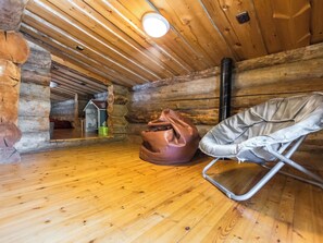 Interior de una cabaña de madera con suelo de madera, un sillón de mimbre marrón y una silla plegable de metal.