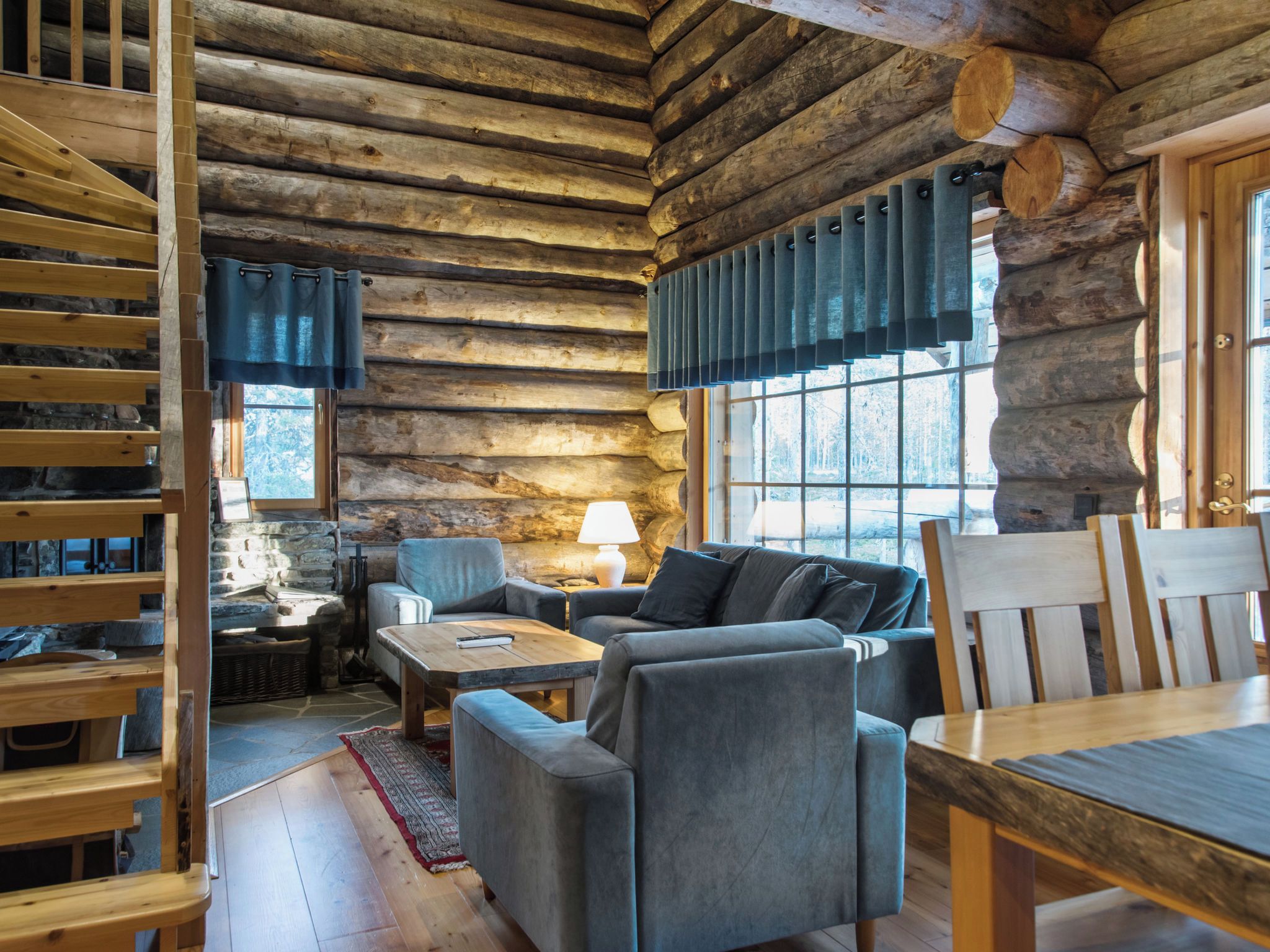 A log cabin interior with a stone fireplace, a sofa set, and a dining table.