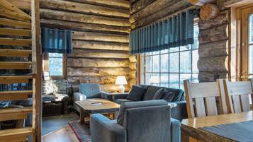 A log cabin interior with a stone fireplace, a sofa set, and a dining table.