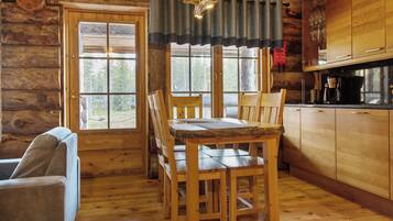 A wooden cabin interior with a dining table, chairs, a sofa, and a kitchen area.