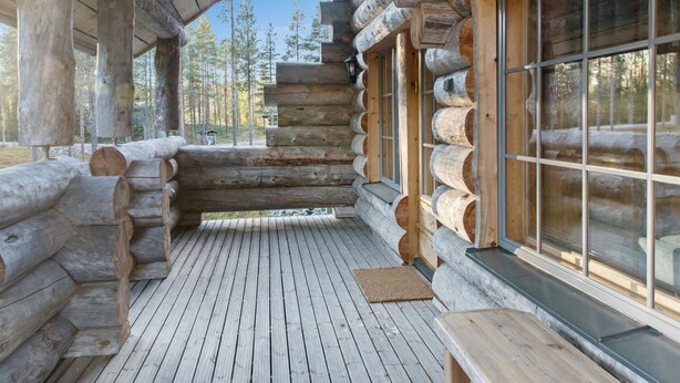 Una cabaña de troncos con terraza de madera, ventanas amplias y vistas al bosque circundante.