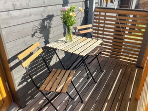 A wooden deck with a table and two chairs, a vase with flowers, and a metal fence. - Karhunvartijan linna a1 by Interhome (Kuusamo)