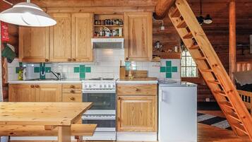 A wooden cabin interior with a kitchen area, including a stove, refrigerator, and wooden cabinets.