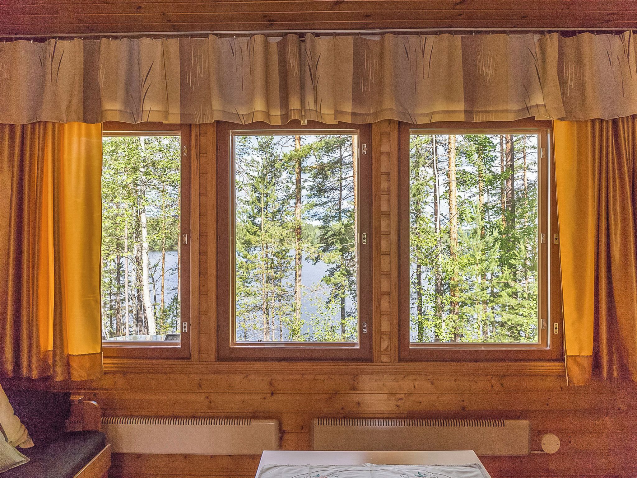 A room with a wooden interior, a window with curtains, and a view of a forest.