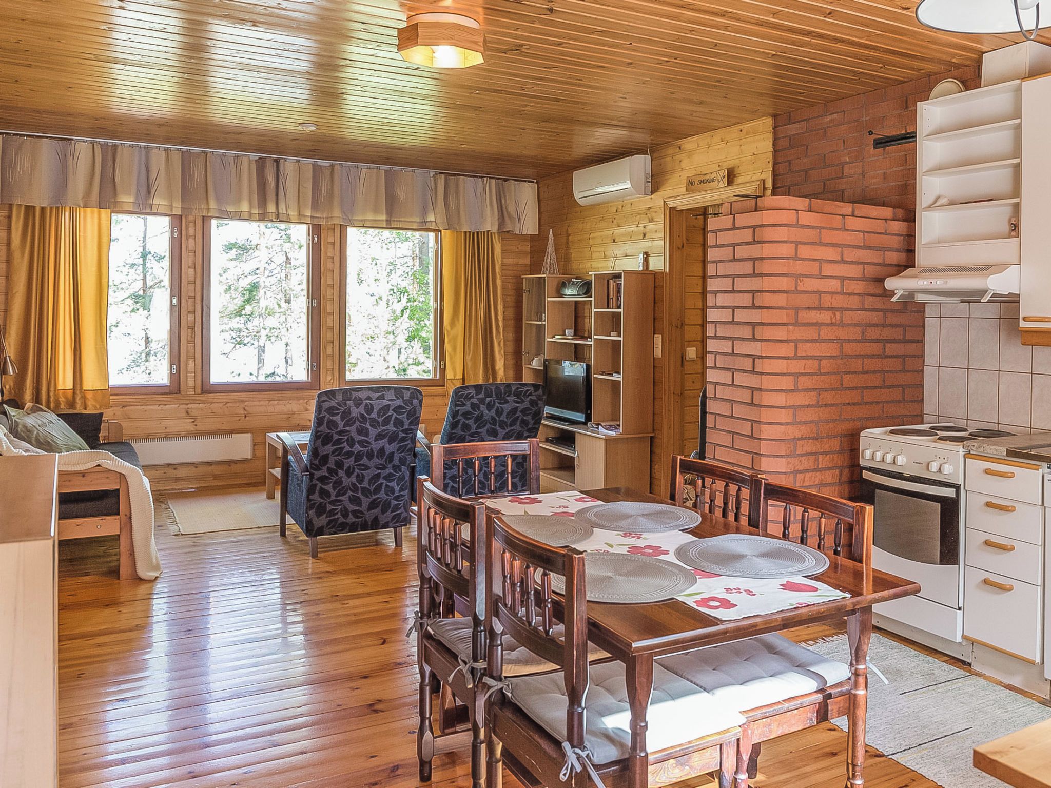 Interior acogedor de una cabaña con una mesa de comedor de madera, sillas, un sofá, un televisor y una pared de ladrillo.