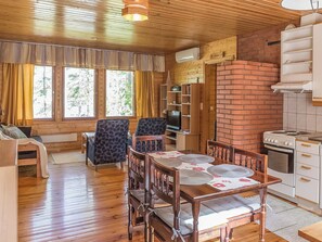 L’intérieur d’un chalet accueillant, avec une table à manger en bois, des chaises, un canapé, un téléviseur et un mur en briques.